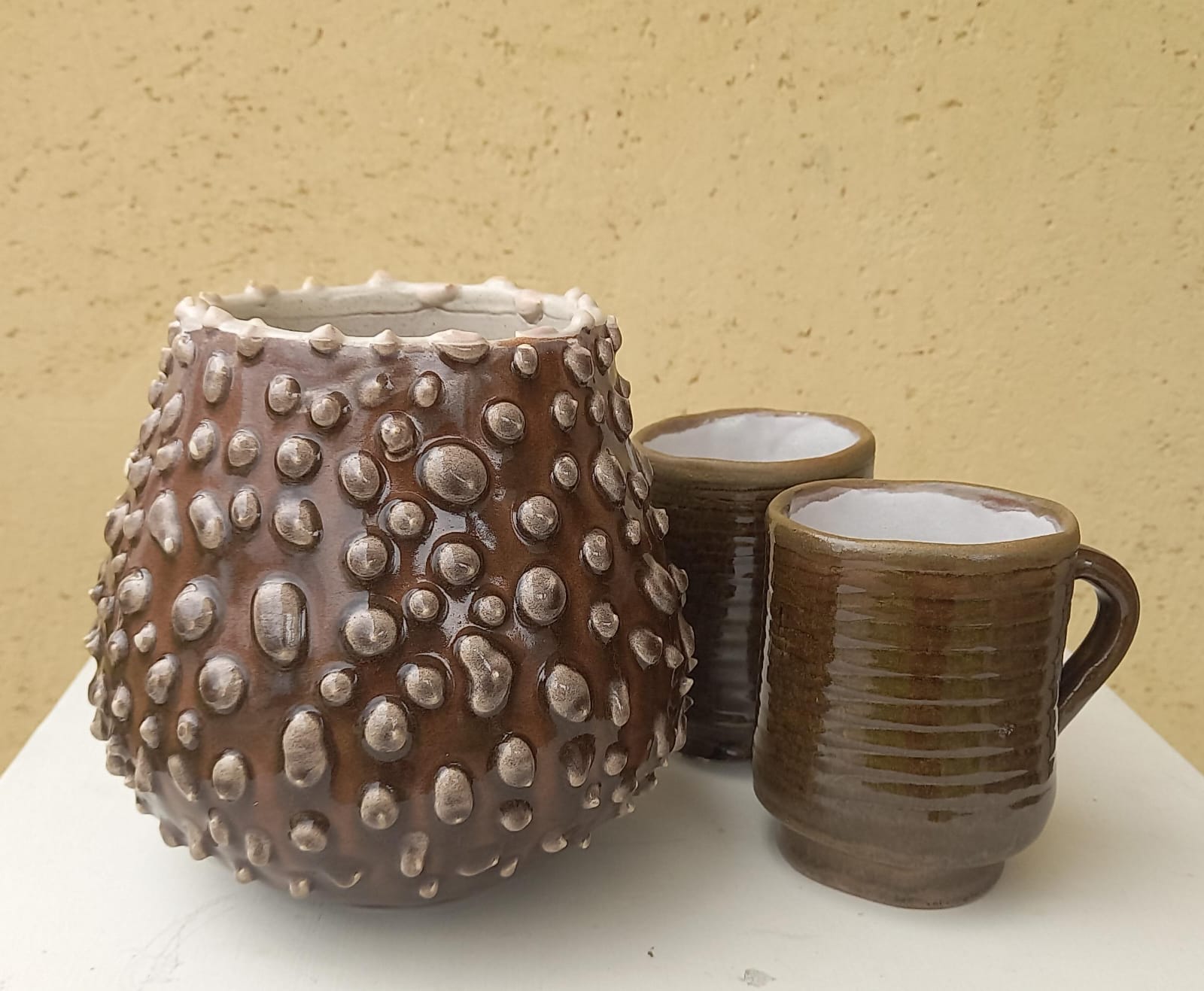 Vaso marrone con rilievi a bolle e due tazze smaltate